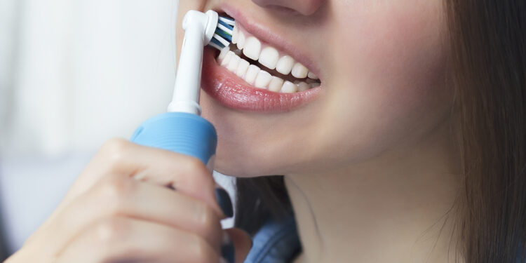 Close up of brushing teeth with electric toothbrush. Young woman